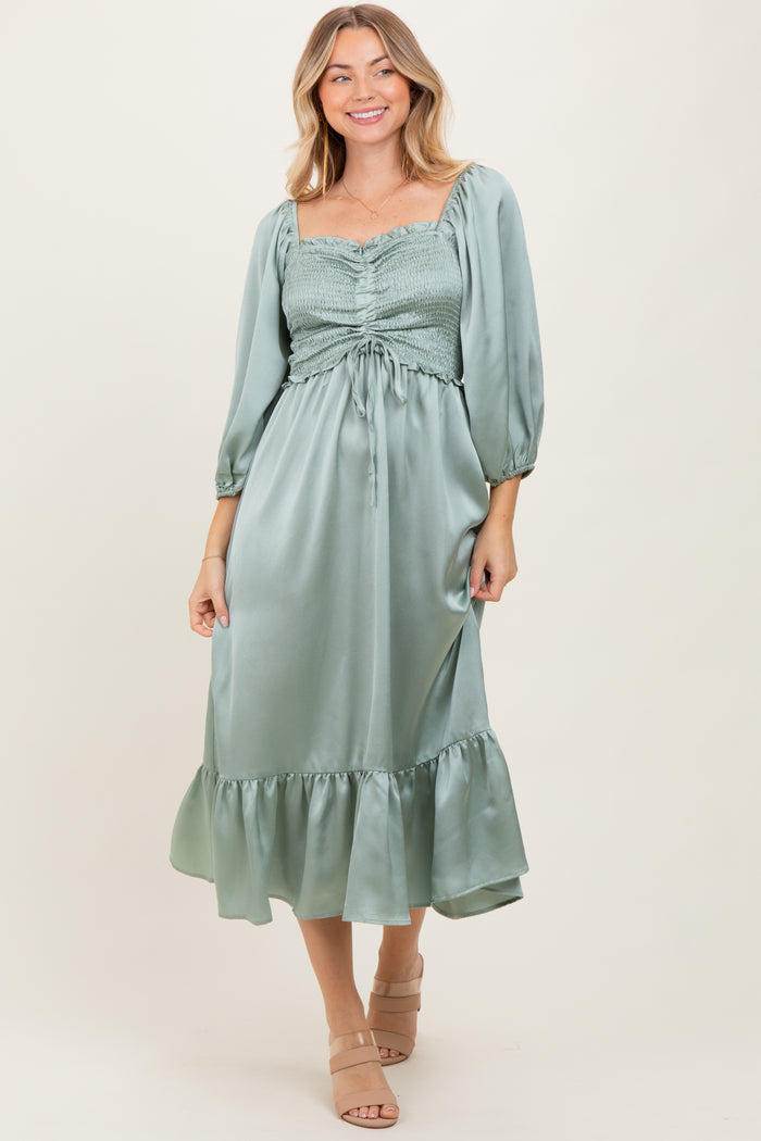woman wearing a sage green midi dress with smocked bodice and puff sleeves, styled with a ruffled hem