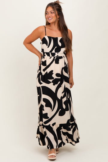woman wearing a black and white floral print maternity maxi dress with a ruffled hem and adjustable straps
