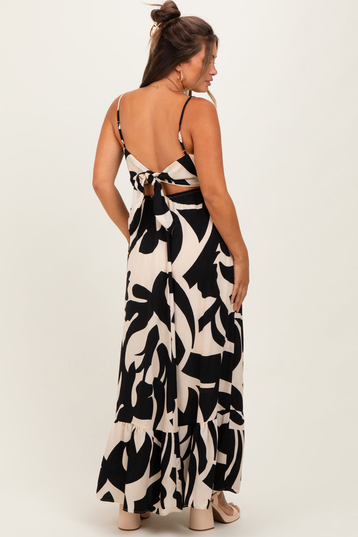 woman wearing a black and cream patterned maternity maxi dress with a back tie detail and a tiered hem