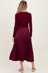 woman wearing a burgundy maternity sweater and pleated maxi skirt, showing a visible baby bump from behind