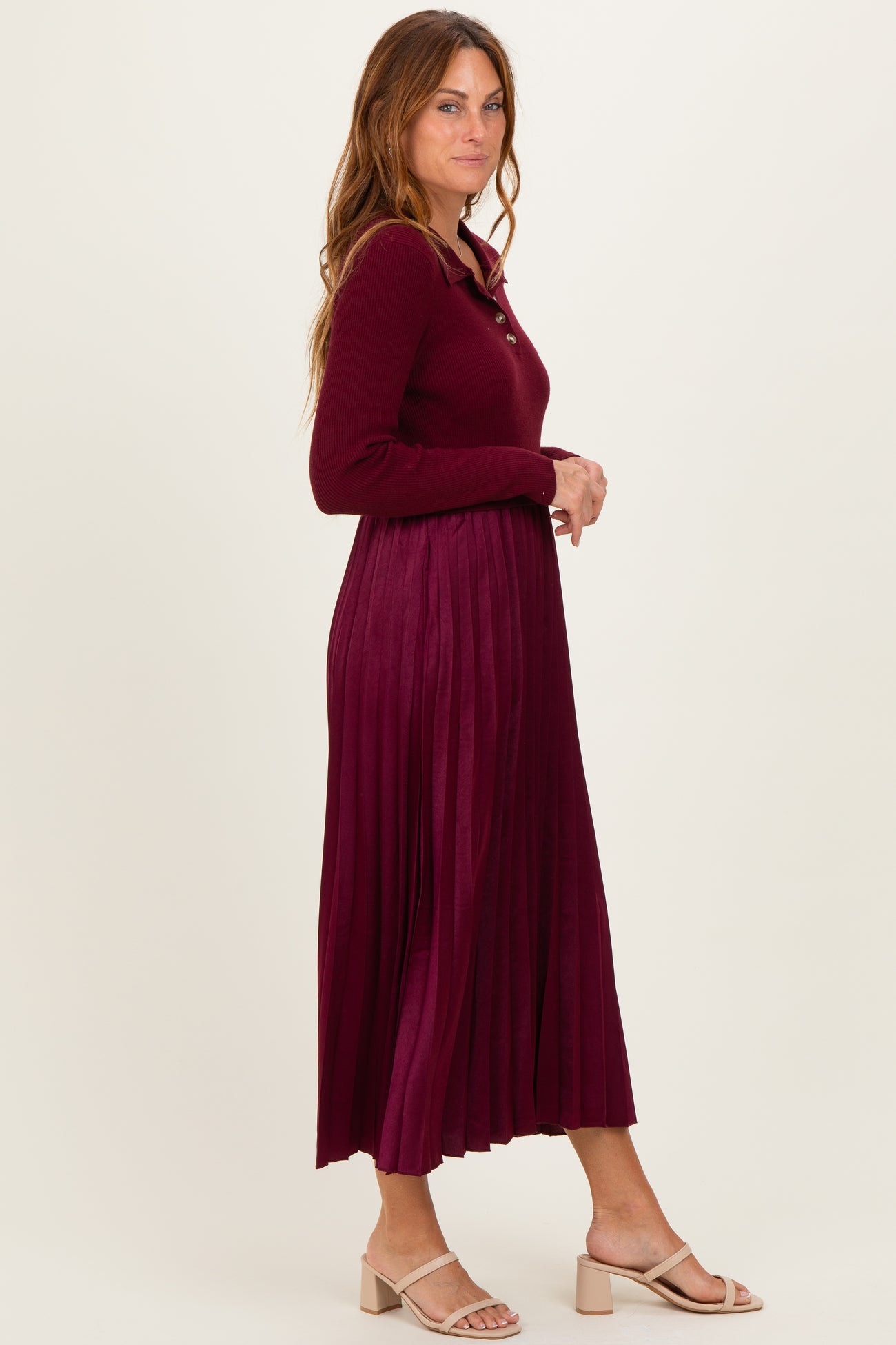 woman wearing a burgundy long sleeve pleated dress with a button-up neckline and heeled sandals