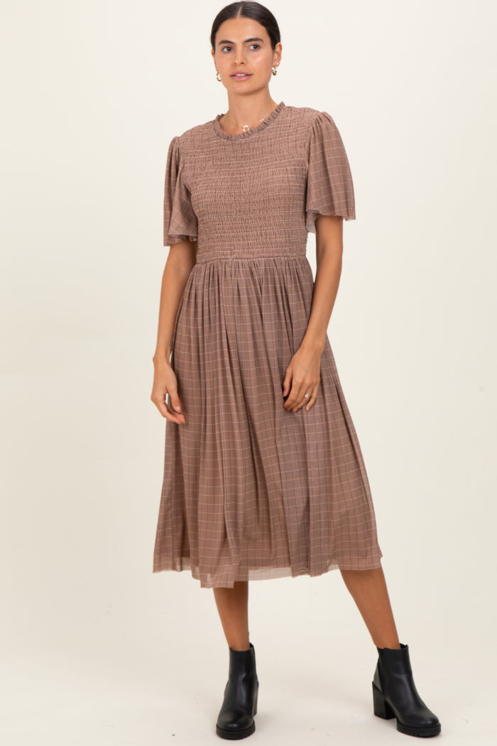 woman wearing a brown checked midi dress with smocked bodice and short puff sleeves, paired with black ankle boots