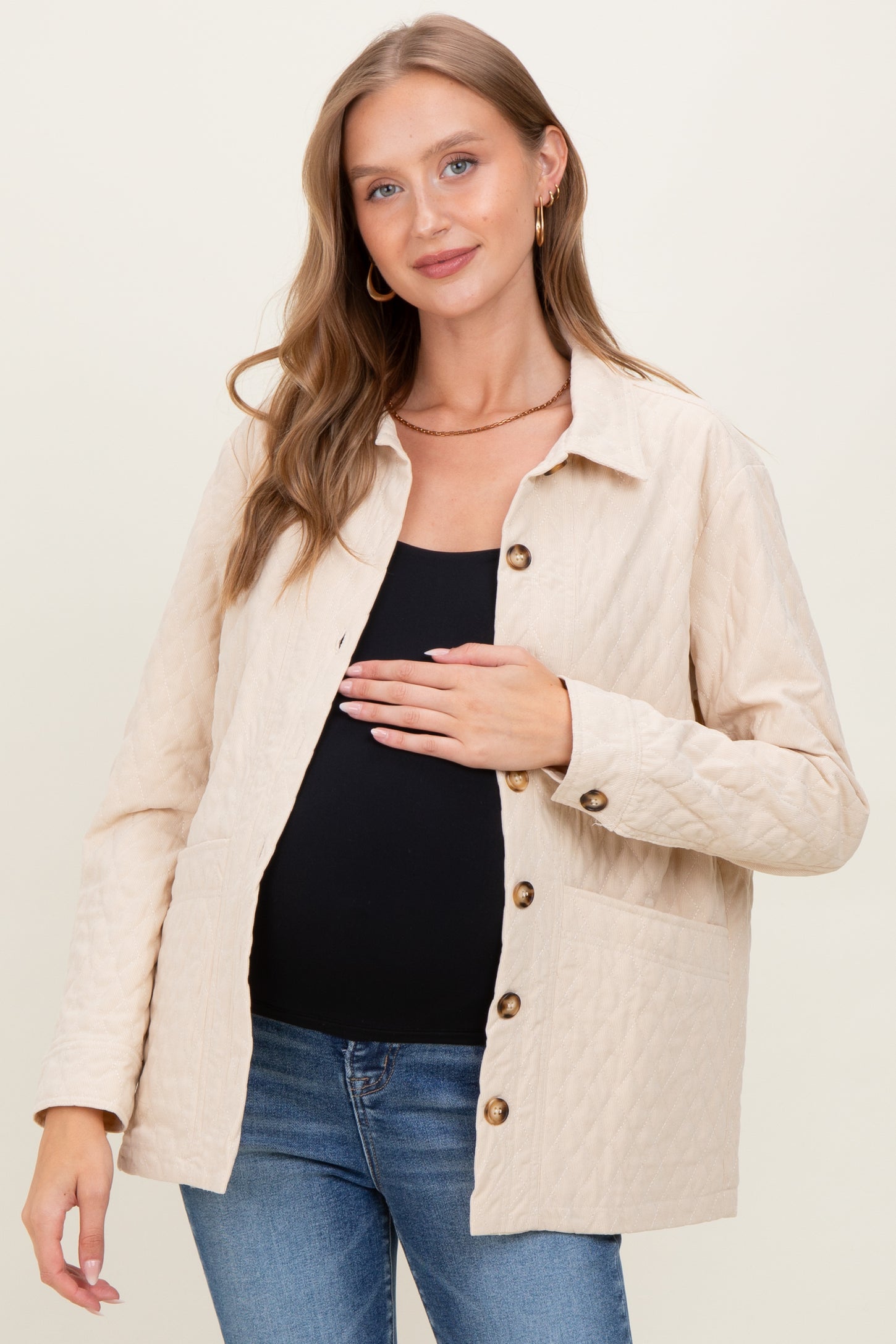 woman wearing a beige quilted maternity jacket and holding her baby bump
