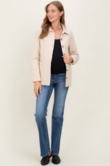 woman wearing a beige maternity jacket over a black top and blue jeans, smiling at the camera