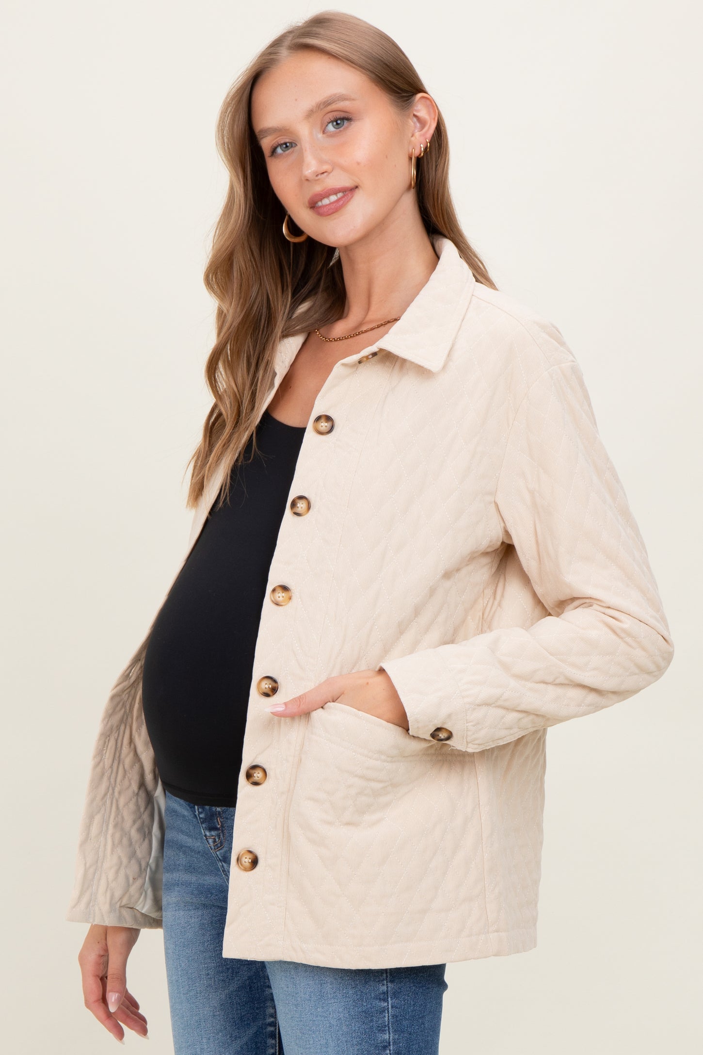 woman wearing a beige quilted maternity jacket with buttons and pockets, showing her baby bump