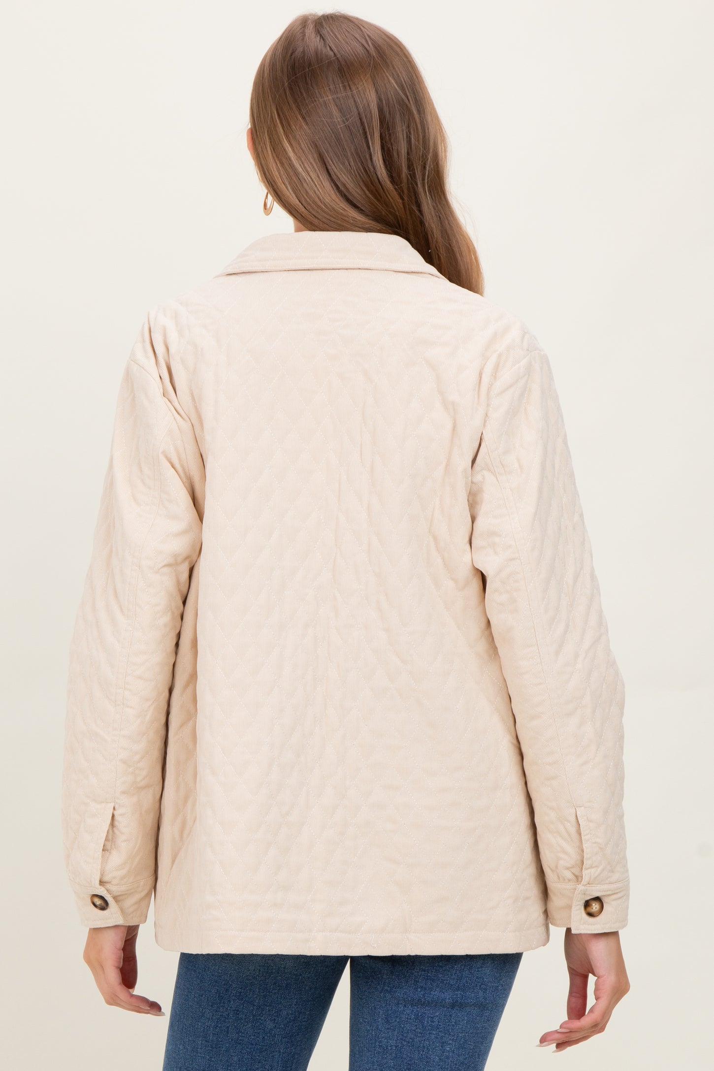 woman wearing a light beige quilted maternity jacket, viewed from the back, with a relaxed fit and button details