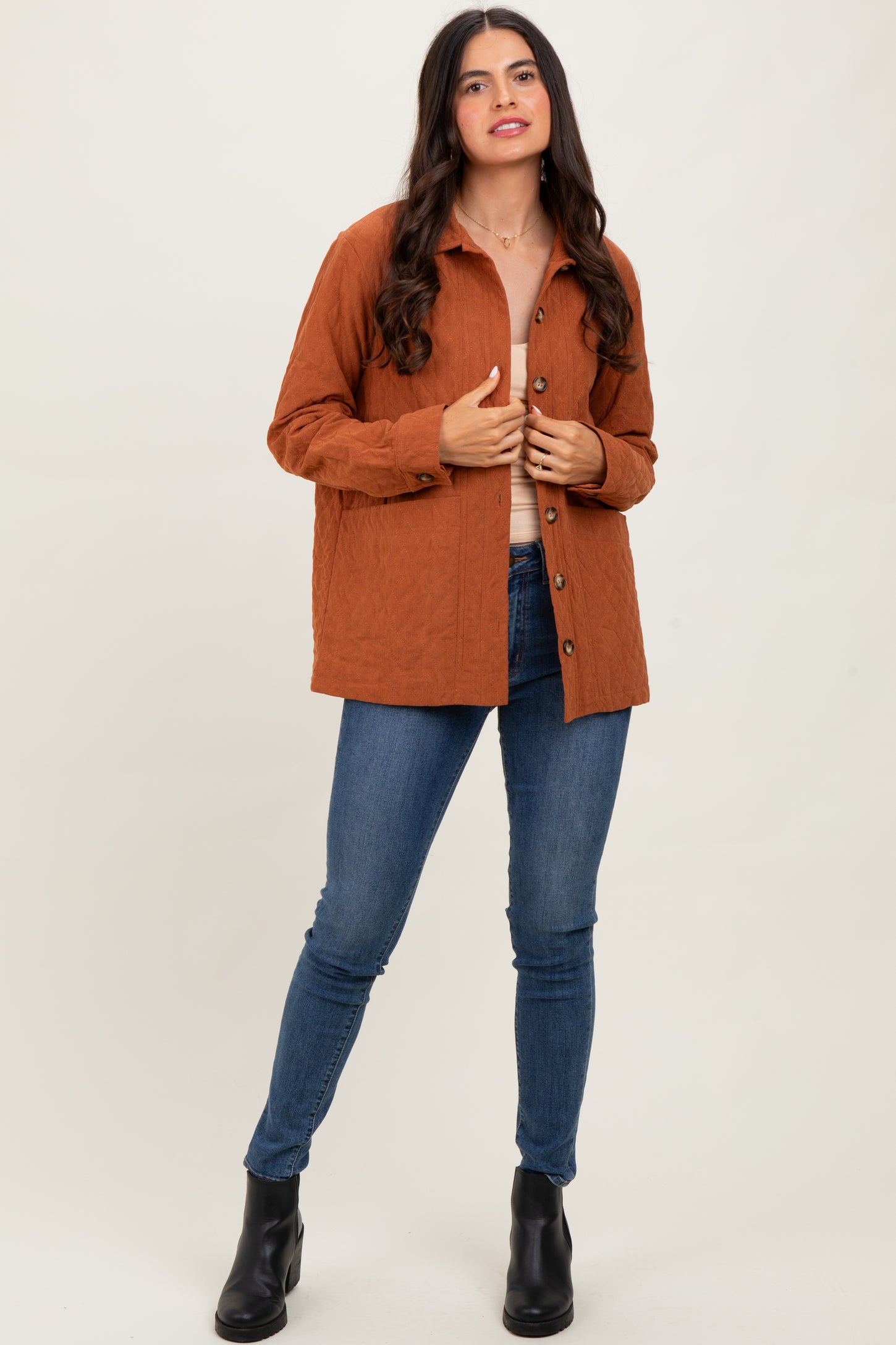 woman wearing an orange textured button-up shirt and blue skinny jeans