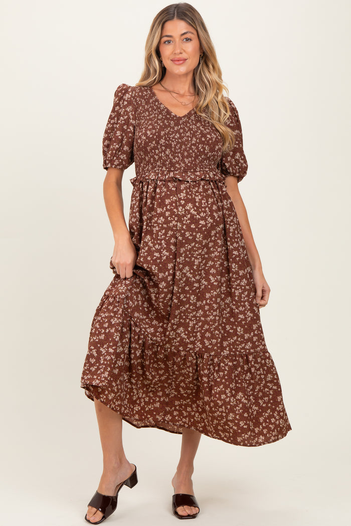 woman wearing a brown floral maternity dress with a v-neckline and puff sleeves, holding the skirt slightly