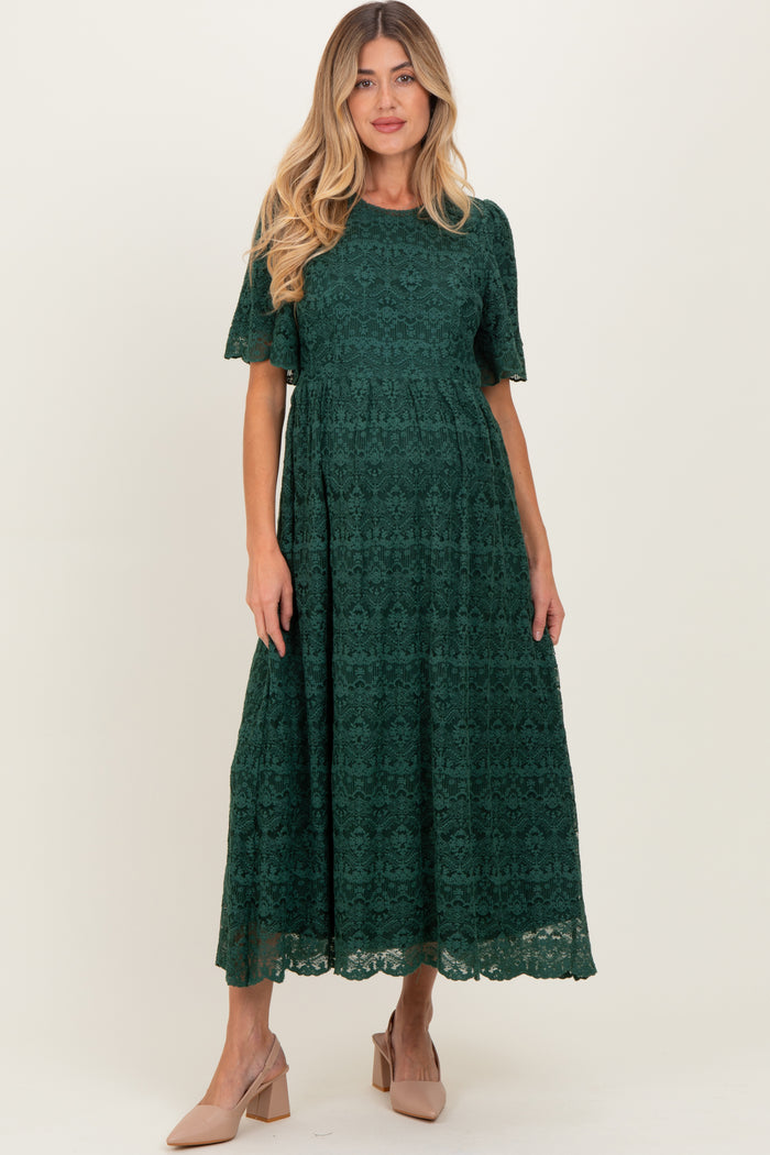 woman wearing a dark green lace short sleeve maternity dress with a flowing skirt and a fitted bodice