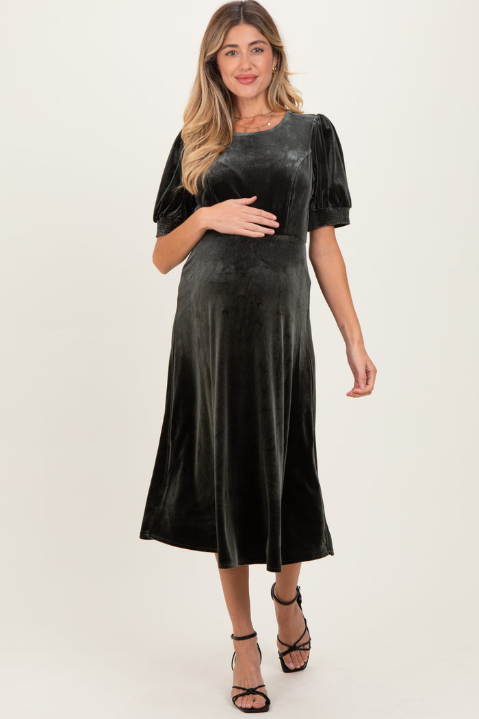 woman wearing a dark green velvet maternity dress with puff sleeves and a baby bump visible