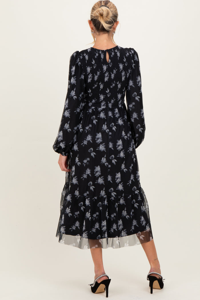 woman wearing a black maternity dress with floral print and sheer ruffled hem, showing the back view