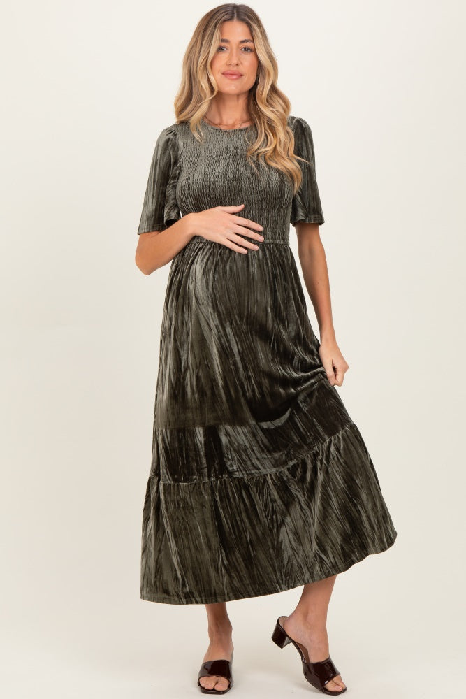 woman wearing a dark green velvet maternity dress with short sleeves and a tiered skirt, holding her baby bump