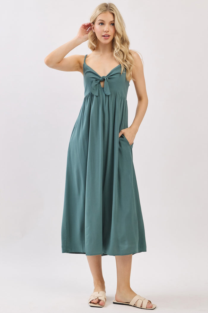 woman wearing a dark green sleeveless midi dress with a keyhole tie detail and side pockets