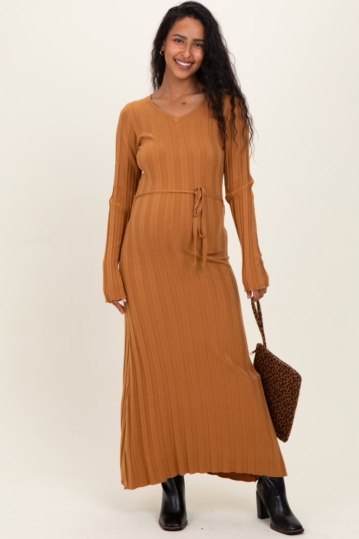 woman wearing a mustard ribbed maternity sweater dress with a tie waist and long sleeves, holding a handbag