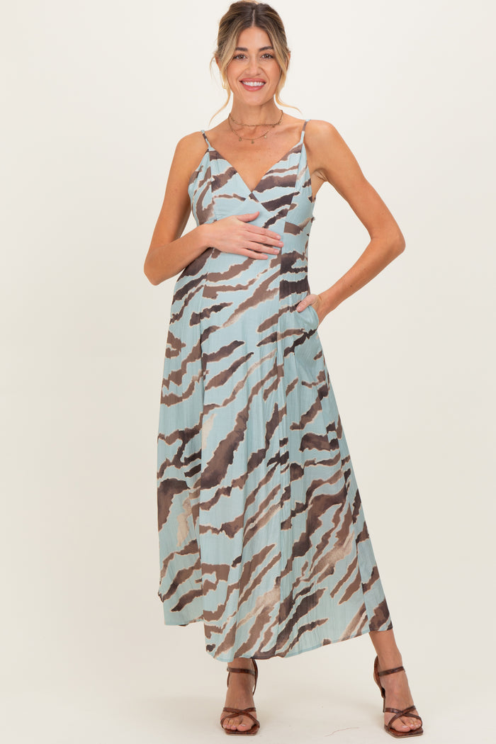 woman wearing a patterned maxi maternity dress in blue and brown, holding her baby bump with a smile