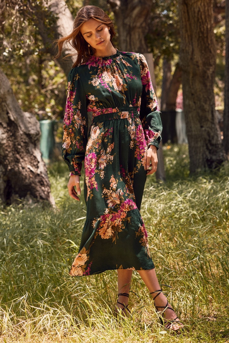 woman wearing a green floral midi dress with long sleeves and a belt, standing in a grassy area outdoors