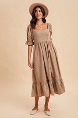 woman wearing a tan square neck midi dress with puff sleeves and ruffle hem, paired with a wide-brim hat and slip-on shoes