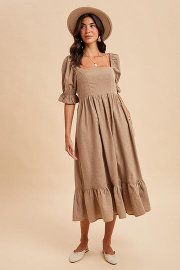 woman wearing a tan square neck midi dress with puff sleeves and ruffle hem, paired with a wide-brim hat and slip-on shoes