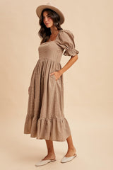 woman wearing a brown puff sleeve midi dress with a ruffled hem and pockets, styled with a tan hat and slip-on shoes