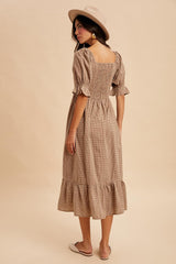woman wearing a beige gingham midi dress with puff sleeves and a ruffled hem, paired with a stylish hat