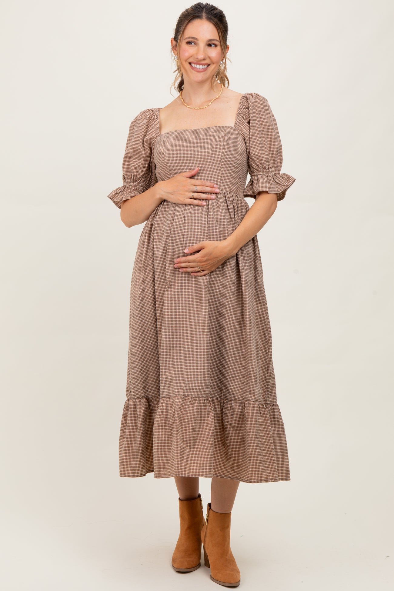 woman wearing a brown checkered maternity dress with puff sleeves and tiered skirt, holding her baby bump