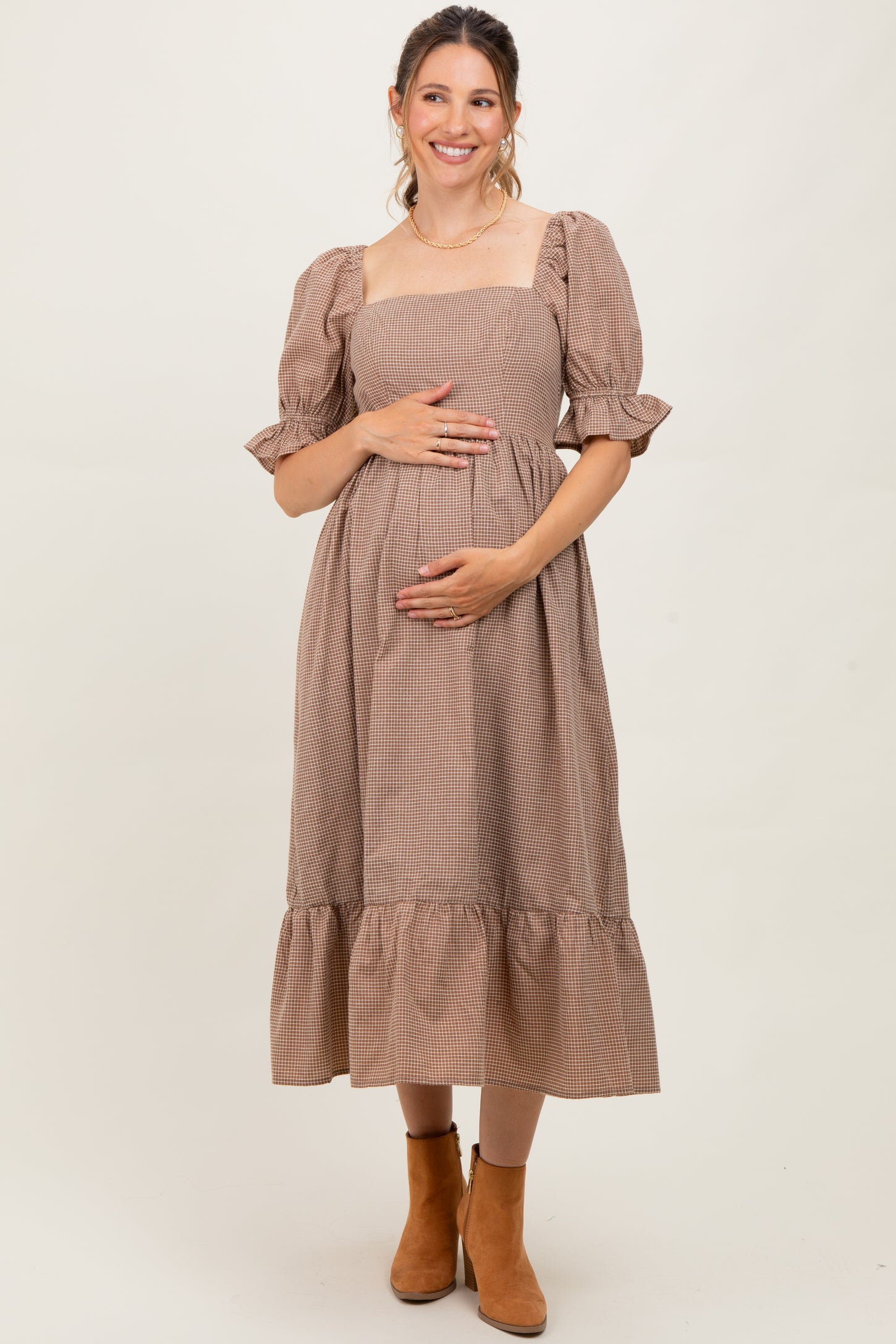 woman wearing a brown checkered maternity dress with puff sleeves and tiered skirt, holding her baby bump