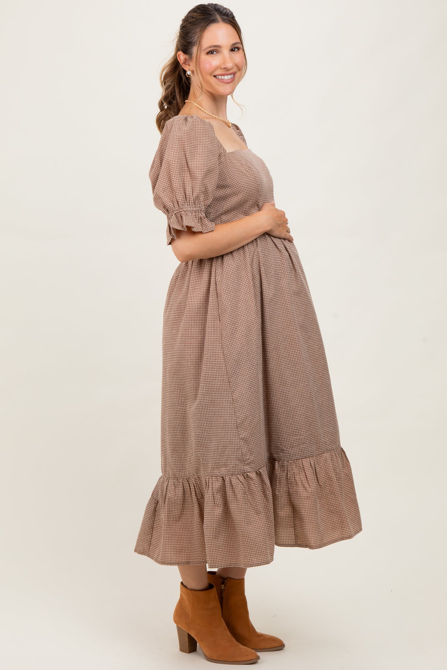 woman wearing a brown checkered maternity dress with puff sleeves and a ruffled hem, showing her baby bump