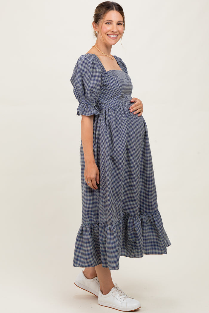 woman wearing a navy and white gingham maternity dress with puff sleeves and a ruffled hem, holding her baby bump