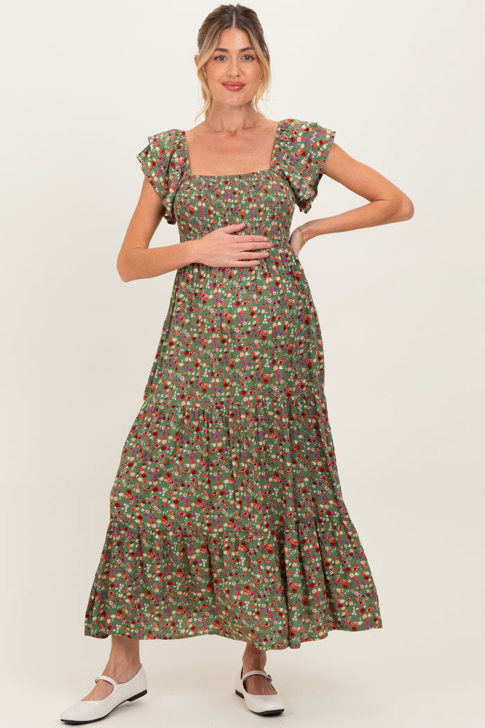 woman wearing a green floral maternity maxi dress with puff sleeves, holding her baby bump