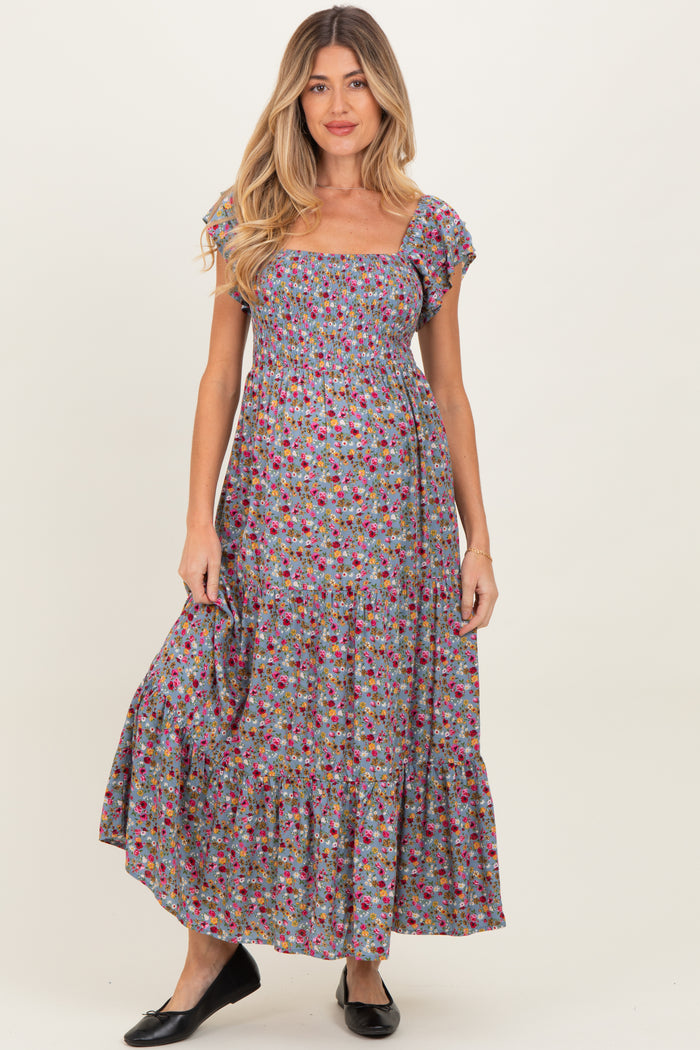 woman wearing a floral maternity maxi dress with short ruffle sleeves and a smocked bodice, featuring a tiered skirt