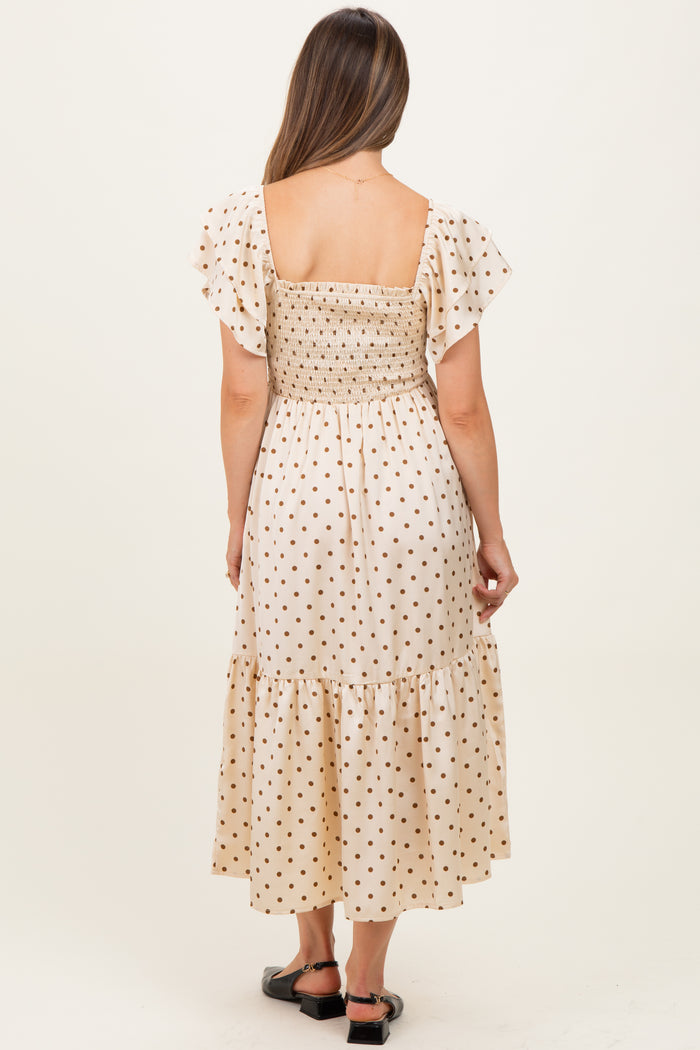 woman wearing a cream polka dot maternity maxi dress with a smocked bodice and flutter sleeves, shown from the back