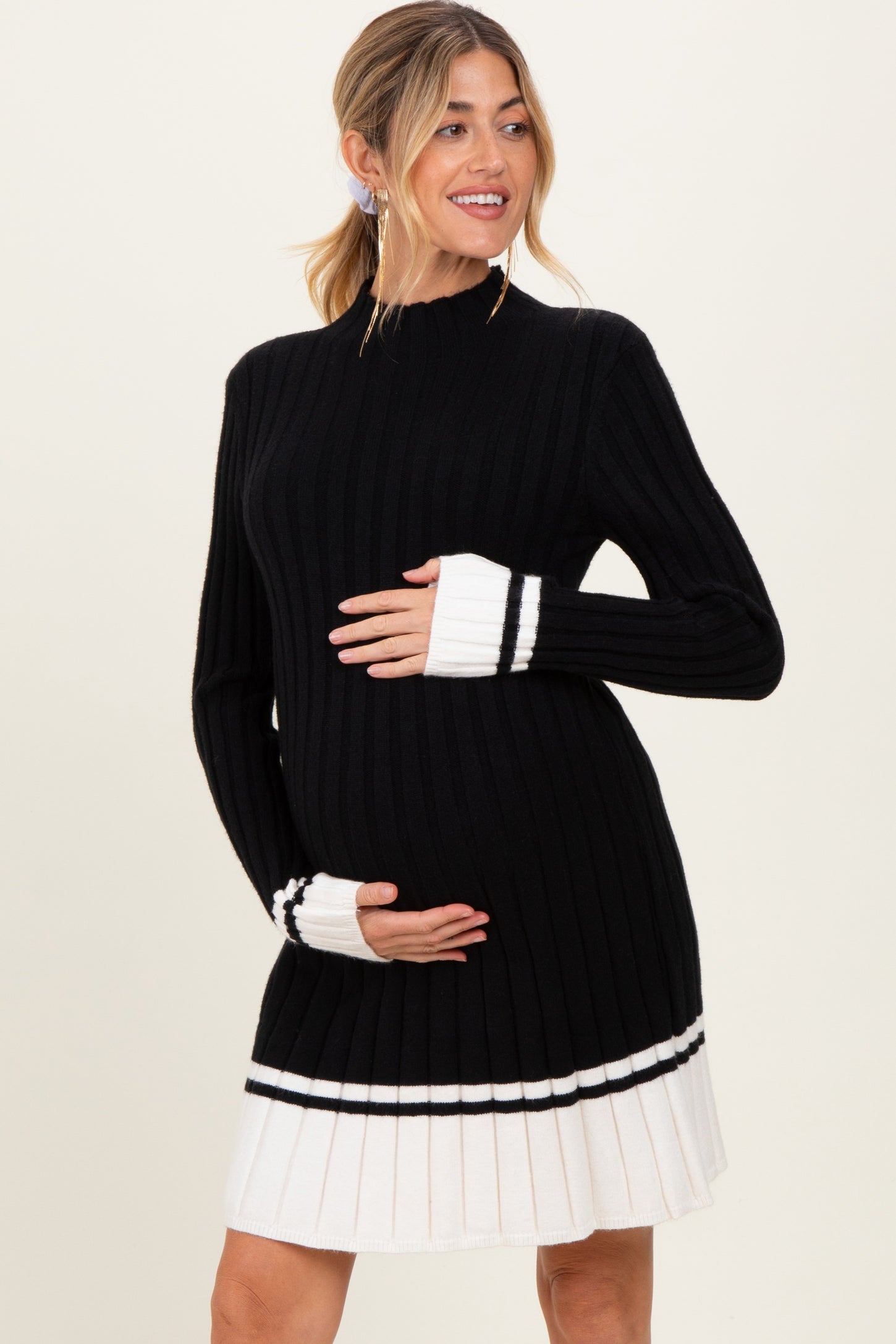 woman wearing a black and white ribbed maternity dress with long sleeves and pleated hem while holding her baby bump