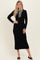 woman wearing a black ribbed midi dress with long sleeves and a striped neck tie, posing against a neutral background