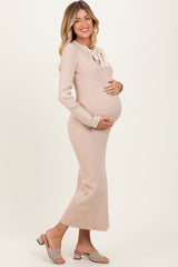 woman wearing a beige ribbed maternity dress with a tie neckline, showing her baby bump and smiling