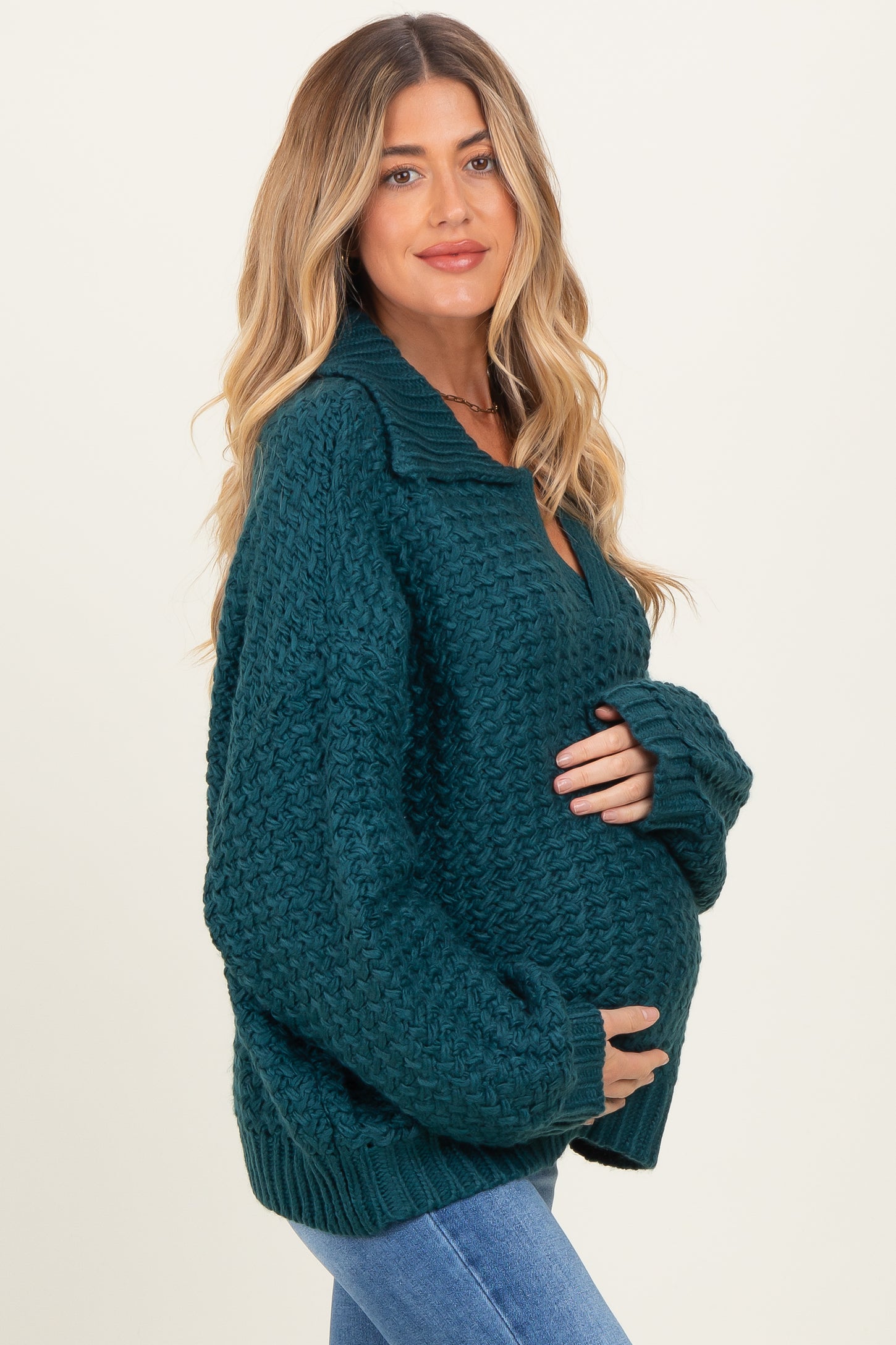 woman wearing a dark green chunky knit maternity sweater and holding her baby bump