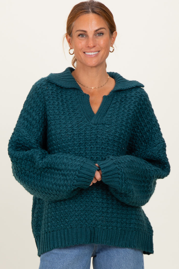woman wearing a teal oversized knitted sweater with a v-neck and a collar, smiling and posing with hands clasped