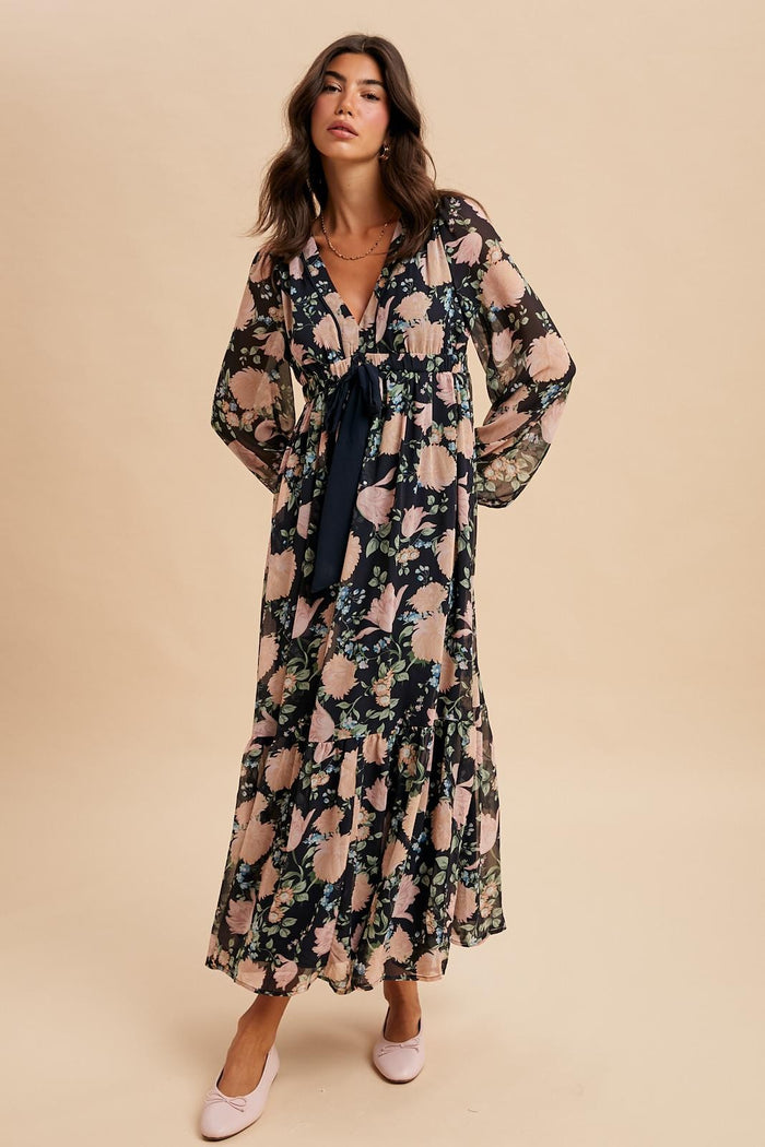 woman wearing a long floral maxi dress with a tie detail and bell sleeves, paired with pink flats