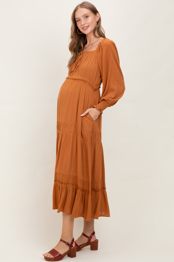 woman wearing a rust colored maternity maxi dress with puff sleeves and a tiered skirt, showing her baby bump