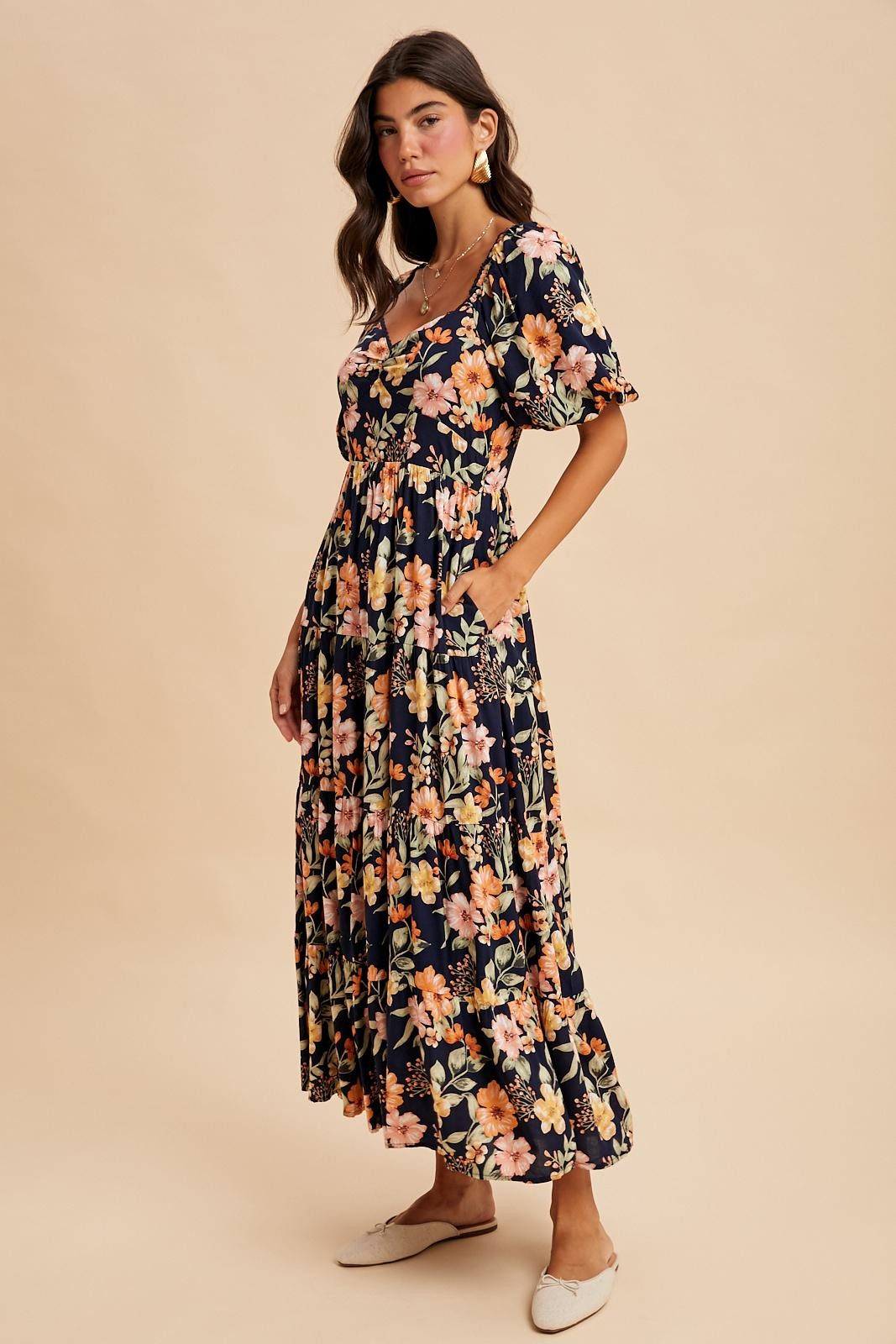 woman wearing a navy floral maxi dress with short sleeves and a tiered skirt, standing in a relaxed pose