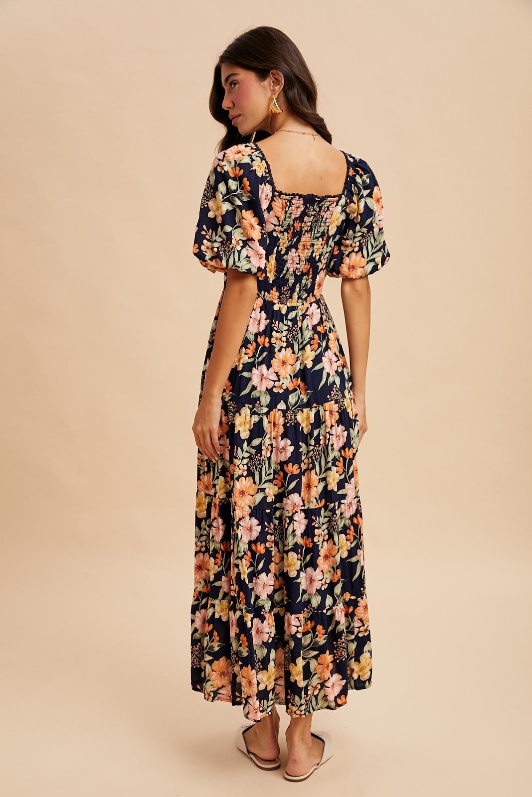 woman wearing a navy floral maxi dress with puff sleeves and a square back, standing with her back to the camera