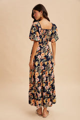 woman wearing a navy floral maxi dress with puff sleeves and a square back, standing with her back to the camera