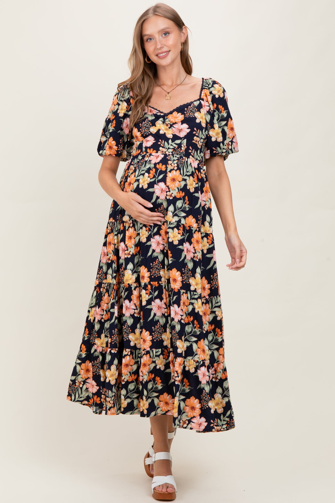woman wearing a black maternity maxi dress with floral print and short puff sleeves, holding her baby bump