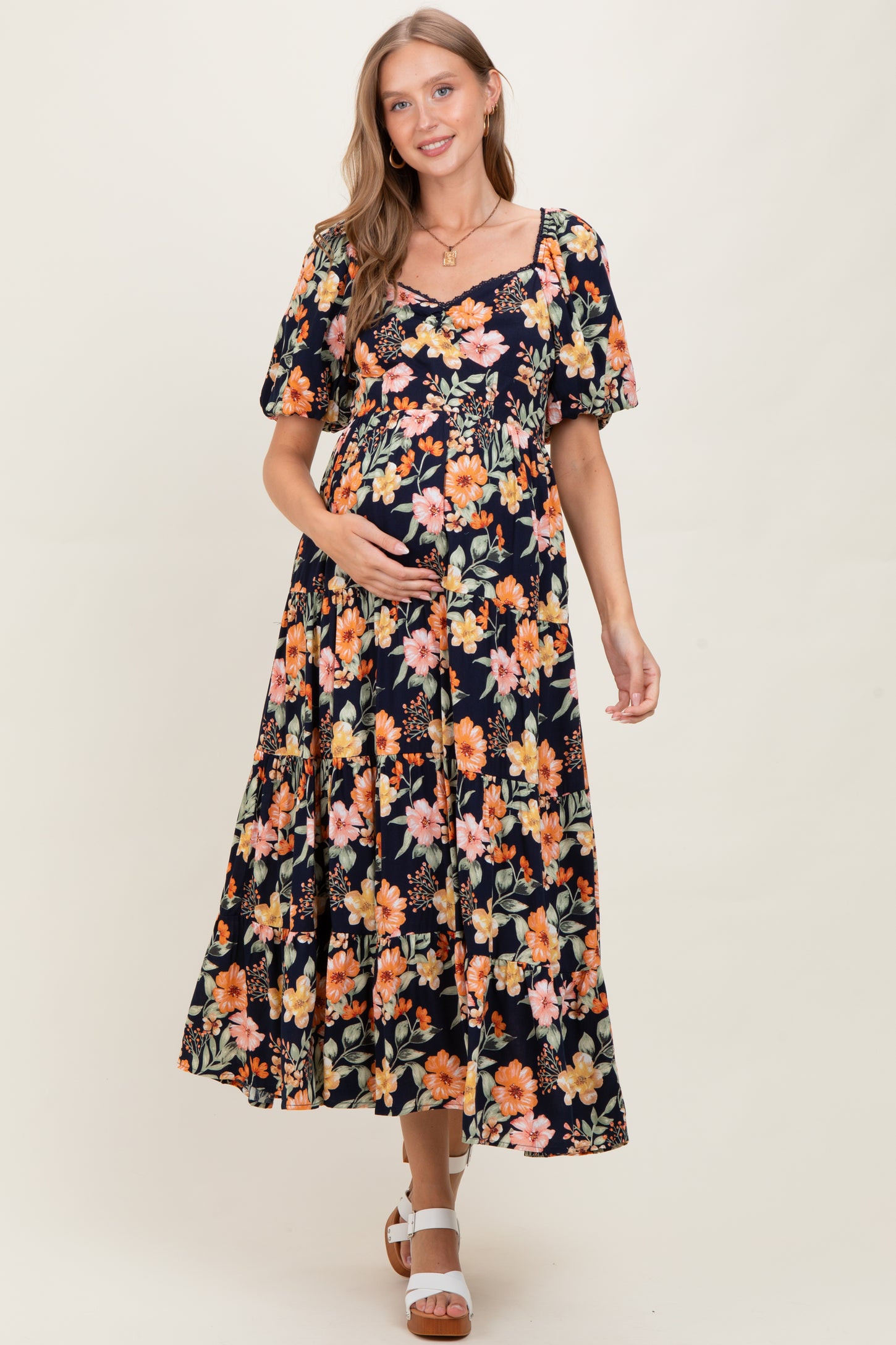 woman wearing a black maternity maxi dress with floral print and short puff sleeves, holding her baby bump