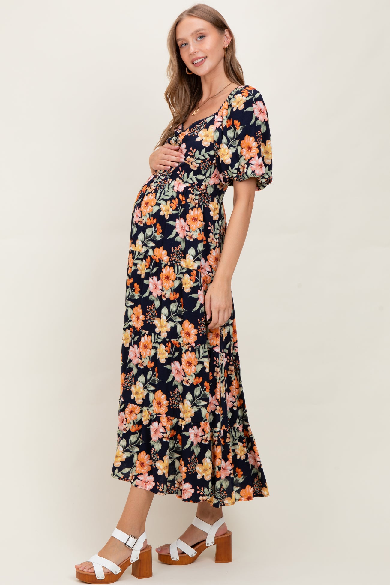 woman wearing a black floral maternity dress with puff sleeves and holding her baby bump