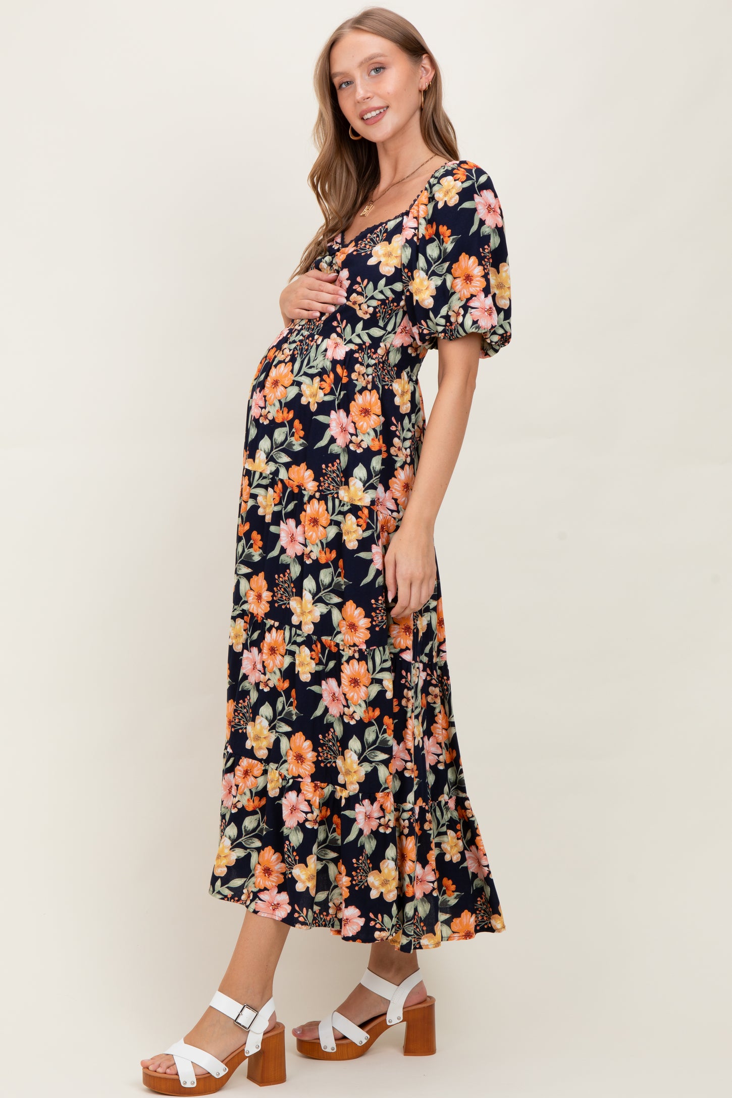 woman wearing a black floral maternity dress with puff sleeves and holding her baby bump