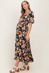 woman wearing a black floral maternity dress with puff sleeves and holding her baby bump