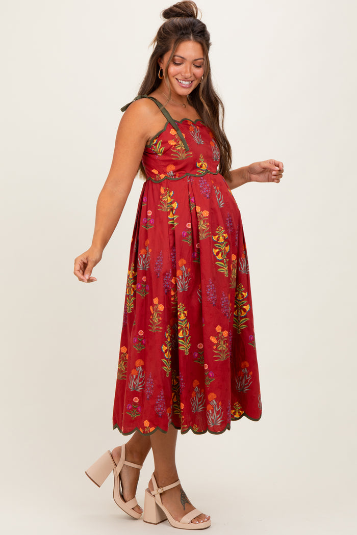 woman wearing a red floral maternity dress with a flowy skirt and a fitted bodice, showcasing her baby bump