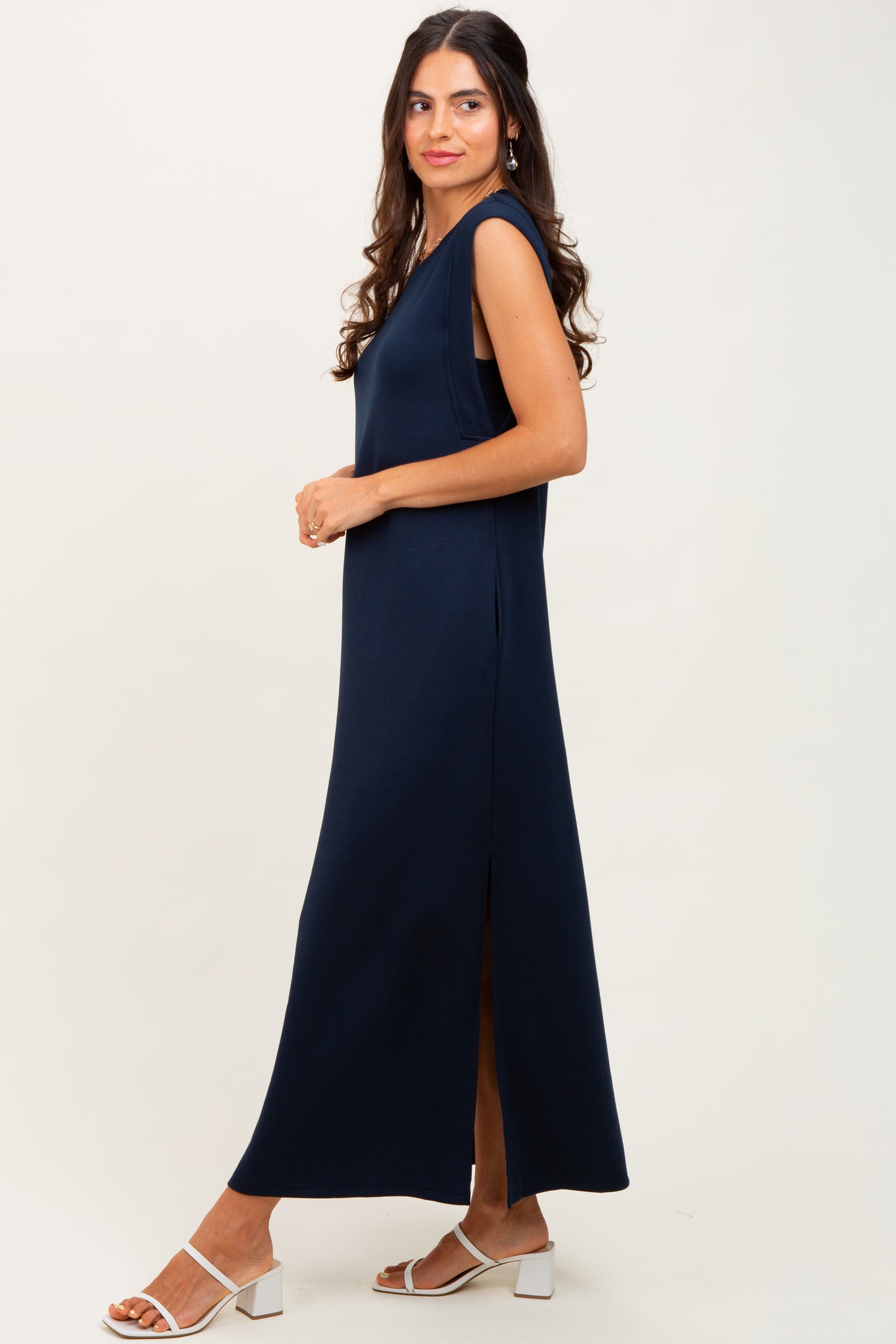 woman wearing a navy blue sleeveless maxi dress with side slits and white heeled sandals