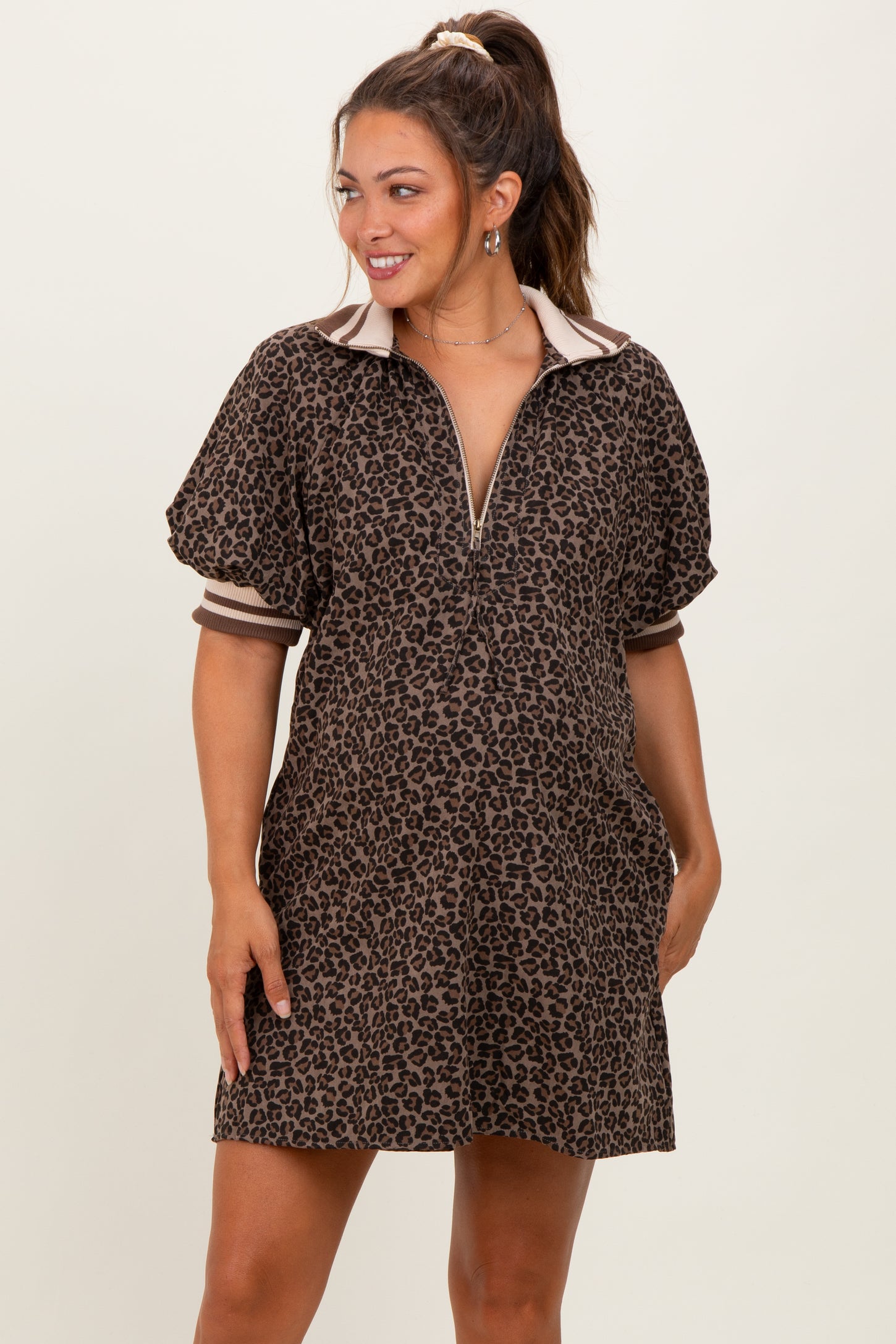 woman wearing a brown leopard print maternity dress with a zip front and short puff sleeves, showing her baby bump