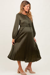 woman wearing an olive green pleated maternity dress with a cinched waist, showcasing her baby bump